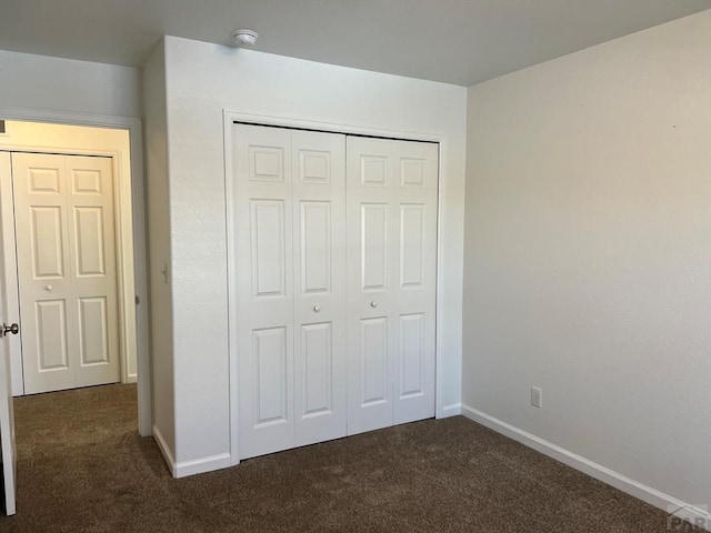 unfurnished bedroom featuring baseboards, dark colored carpet, and a closet