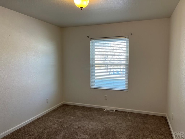 spare room featuring baseboards, visible vents, and dark carpet