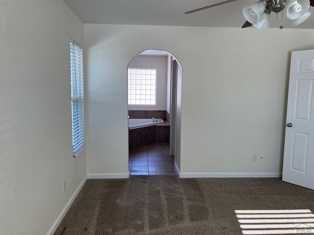 spare room featuring a ceiling fan, arched walkways, dark carpet, and baseboards