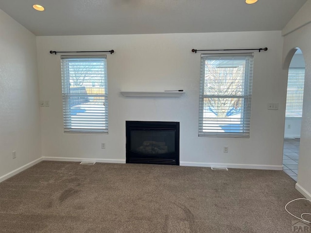 unfurnished living room featuring a glass covered fireplace, plenty of natural light, carpet flooring, and baseboards