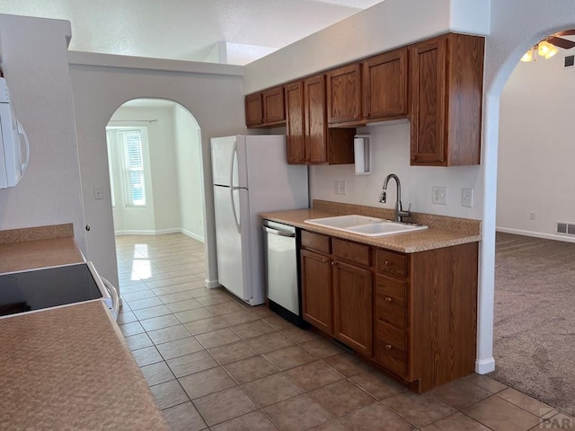 kitchen with brown cabinetry, white appliances, light countertops, and a sink