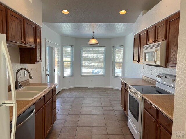 kitchen with hanging light fixtures, white appliances, light countertops, and a sink