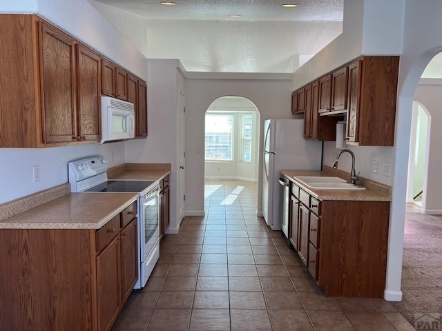 kitchen featuring white appliances, arched walkways, light countertops, and a sink