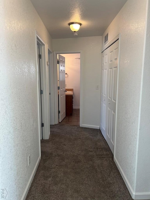 corridor with dark colored carpet, visible vents, a textured wall, a textured ceiling, and baseboards