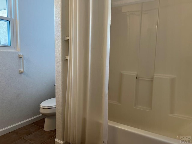 bathroom with washtub / shower combination, tile patterned flooring, baseboards, and toilet