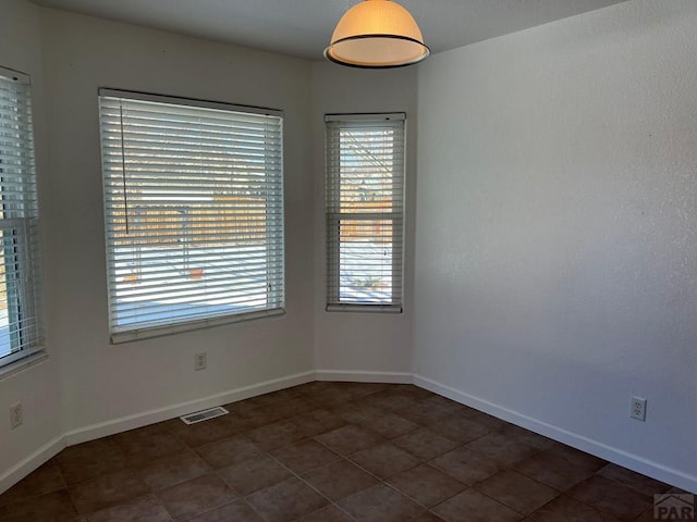 empty room with dark tile patterned flooring, visible vents, and baseboards