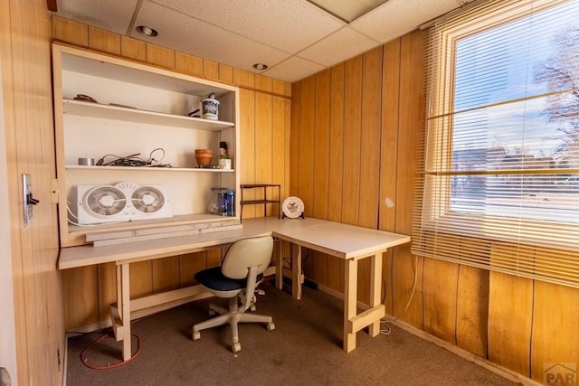 office space featuring built in shelves, wooden walls, a drop ceiling, and carpet flooring