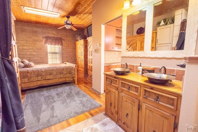 ensuite bathroom featuring wooden ceiling, a sink, and brick wall