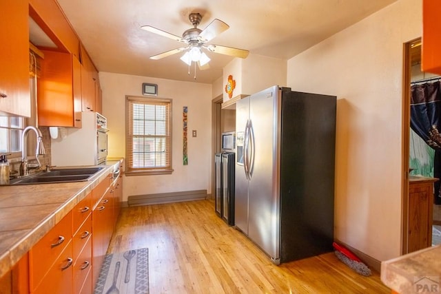 kitchen featuring appliances with stainless steel finishes, brown cabinets, a sink, and light wood finished floors