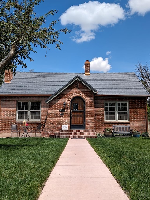 view of front of house with a chimney, a front lawn, and brick siding