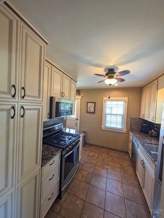 kitchen with dark stone counters, appliances with stainless steel finishes, cream cabinets, and a ceiling fan