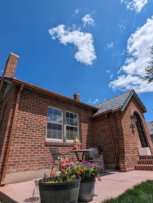 exterior space with a patio area, brick siding, and a chimney