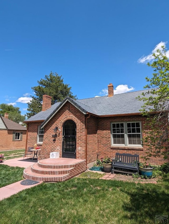 ranch-style home featuring a patio, brick siding, a chimney, and a front yard