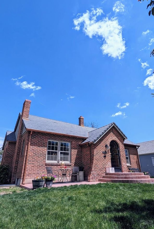 ranch-style home featuring a patio area, brick siding, a chimney, and a front lawn