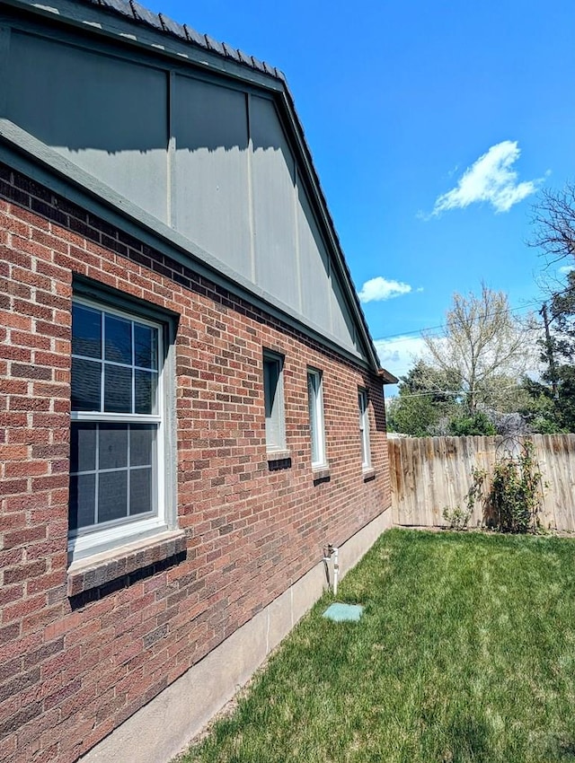 view of side of home with brick siding, a lawn, and fence