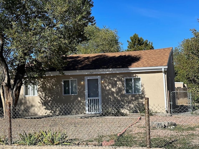 bungalow-style home with a shingled roof, fence, and stucco siding