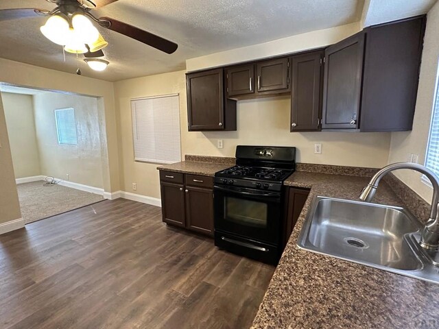 kitchen with dark wood finished floors, dark countertops, black gas range, a sink, and a textured ceiling