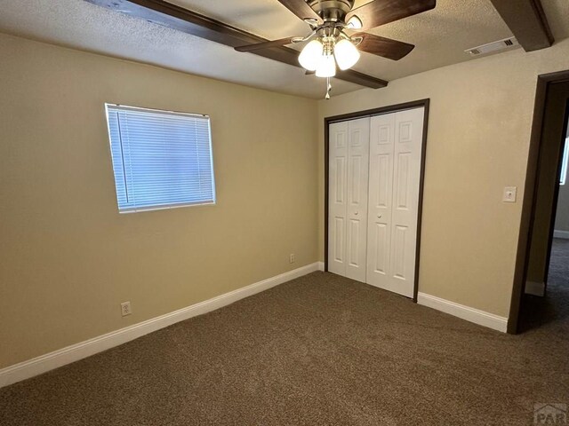 unfurnished bedroom featuring baseboards, visible vents, a textured ceiling, dark carpet, and a closet