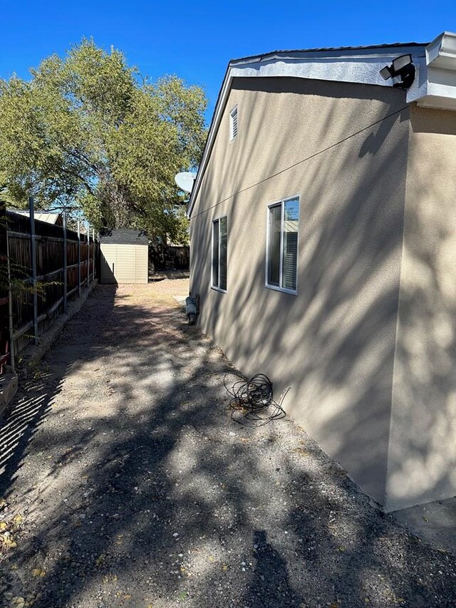 view of side of property with an outbuilding, stucco siding, fence, and a shed