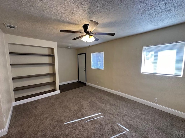 unfurnished bedroom featuring baseboards, visible vents, ceiling fan, a textured ceiling, and dark carpet