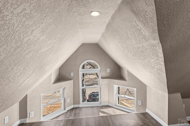 bonus room featuring baseboards, a textured wall, wood finished floors, vaulted ceiling, and a textured ceiling