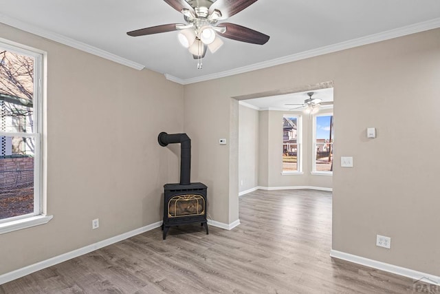 unfurnished room with a wood stove, light wood-style floors, baseboards, and ornamental molding