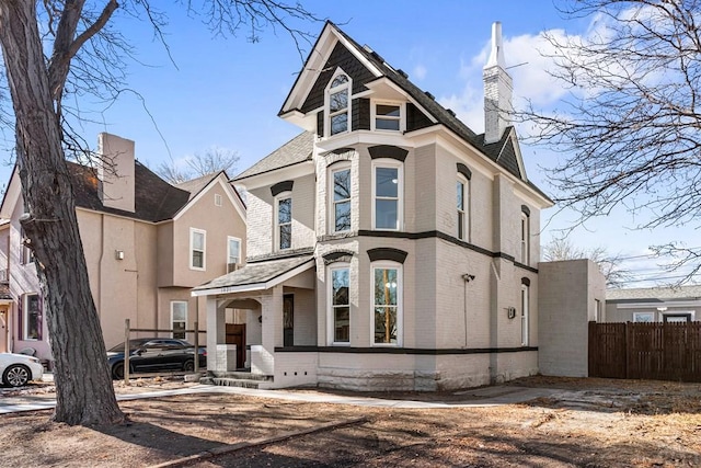 victorian home with brick siding, fence, and a chimney