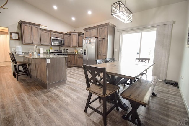 kitchen featuring appliances with stainless steel finishes, wood finished floors, a peninsula, light stone countertops, and hanging light fixtures