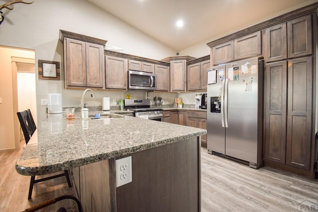 kitchen featuring a peninsula, vaulted ceiling, appliances with stainless steel finishes, light stone countertops, and a kitchen bar