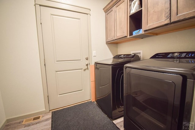 laundry area featuring cabinet space, visible vents, light wood-type flooring, independent washer and dryer, and baseboards