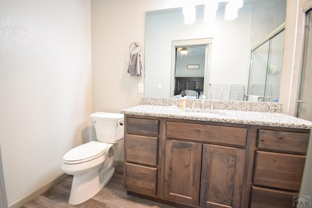 ensuite bathroom featuring connected bathroom, toilet, a shower with shower door, vanity, and baseboards