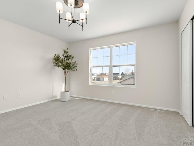 carpeted empty room featuring visible vents, a notable chandelier, and baseboards