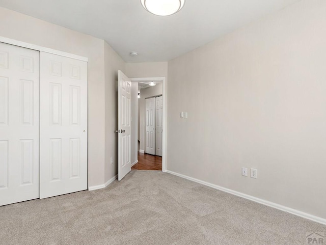 unfurnished bedroom featuring a closet, light carpet, and baseboards