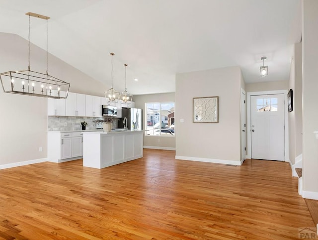 kitchen with stainless steel appliances, light countertops, hanging light fixtures, open floor plan, and white cabinets