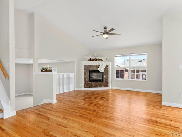 unfurnished living room with ceiling fan, wood finished floors, a high end fireplace, baseboards, and vaulted ceiling