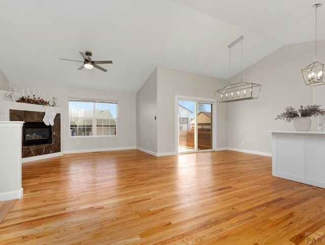 unfurnished living room with baseboards, a premium fireplace, vaulted ceiling, light wood-type flooring, and ceiling fan with notable chandelier