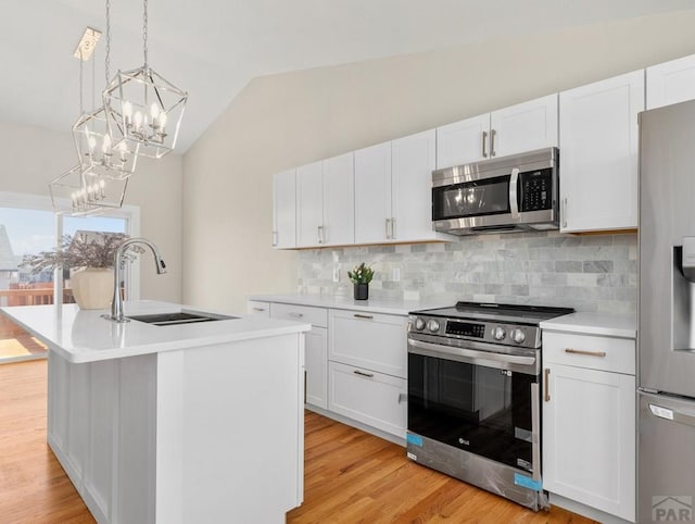 kitchen with decorative light fixtures, stainless steel appliances, light countertops, a sink, and an island with sink