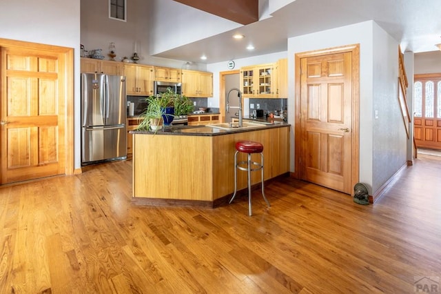 kitchen with dark countertops, glass insert cabinets, a peninsula, stainless steel appliances, and light wood-style floors