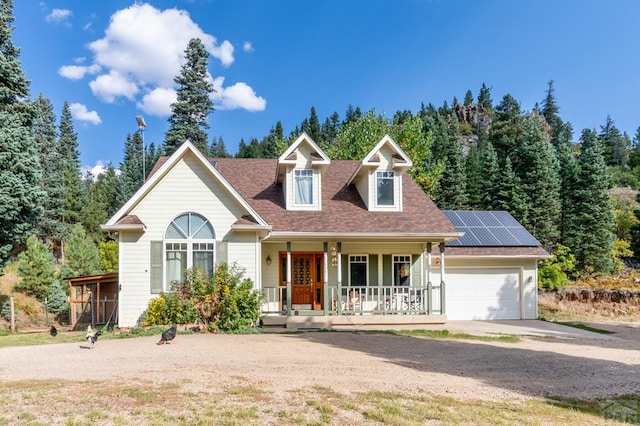 view of front of home with an attached garage, covered porch, solar panels, concrete driveway, and roof with shingles