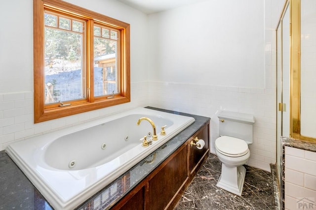 bathroom with wainscoting, toilet, tile walls, and a tub with jets