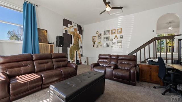 carpeted living room featuring a ceiling fan, arched walkways, and stairs