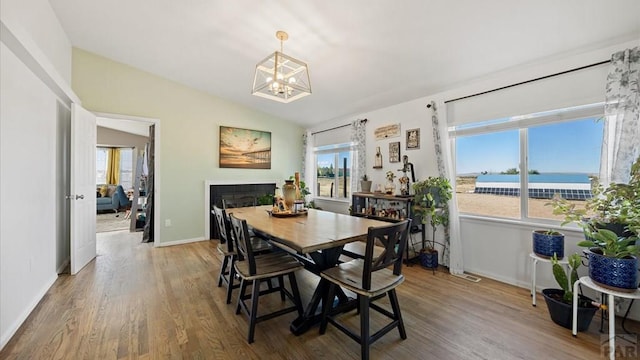 dining room featuring wood finished floors, a notable chandelier, vaulted ceiling, and a fireplace