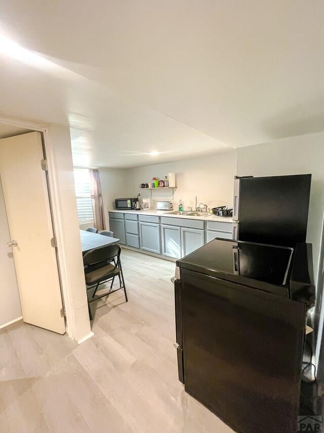 kitchen featuring light wood finished floors, gray cabinets, light countertops, freestanding refrigerator, and a sink