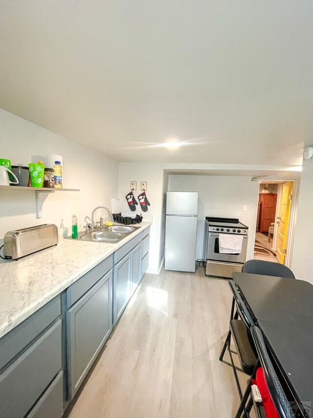 kitchen featuring light wood finished floors, electric stove, light stone counters, freestanding refrigerator, and a sink