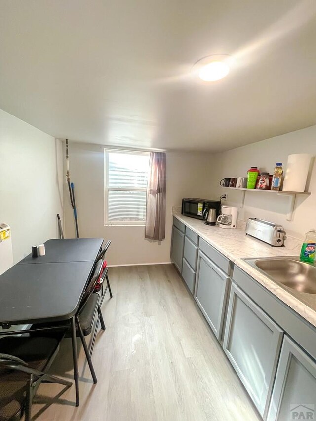 kitchen with a sink, light countertops, light wood-type flooring, gray cabinets, and open shelves