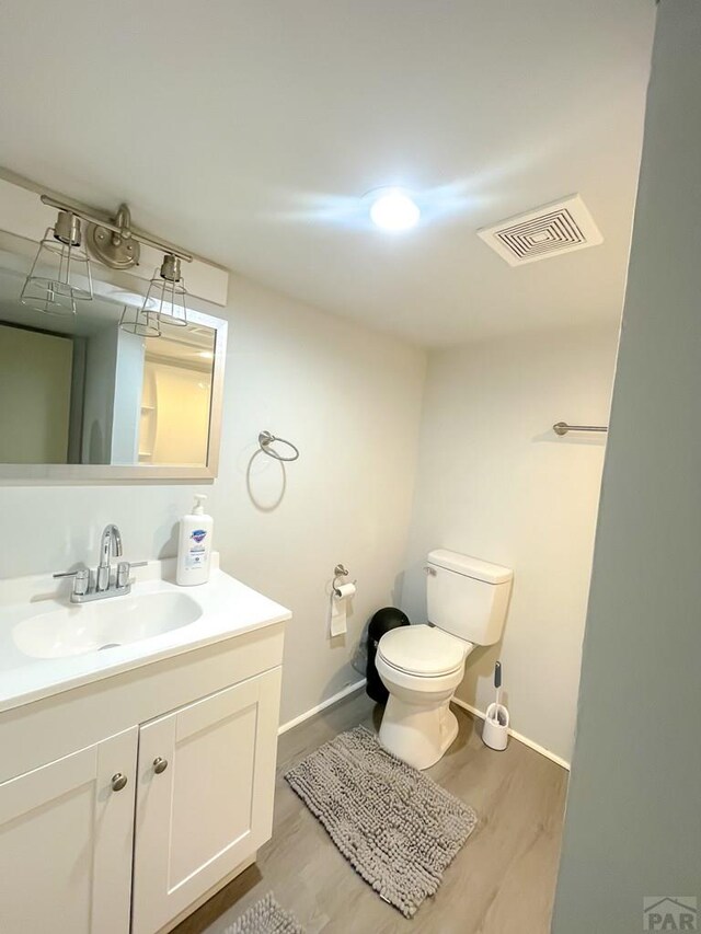 half bathroom with toilet, wood finished floors, vanity, and visible vents