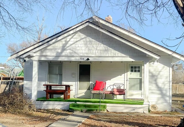 view of front of house featuring covered porch, a chimney, and fence