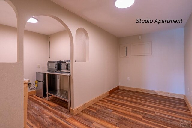 interior space featuring arched walkways, wood finished floors, and baseboards