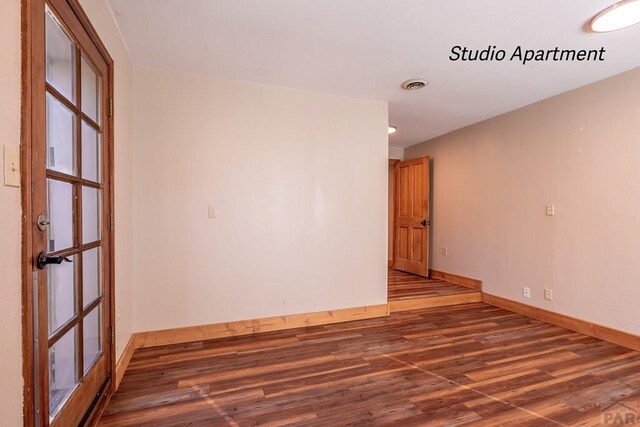 unfurnished room with dark wood-style floors, visible vents, and baseboards