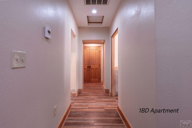 hall featuring attic access, visible vents, baseboards, and wood finished floors